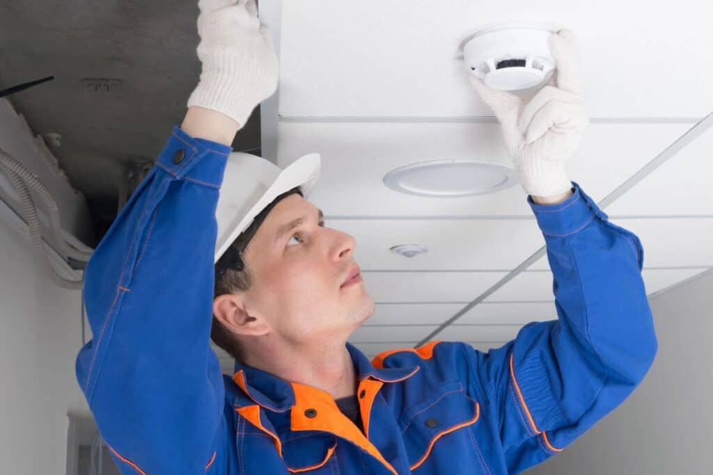 Home electrician fitting smoke alarm unit on ceiling in Bullcreek Home