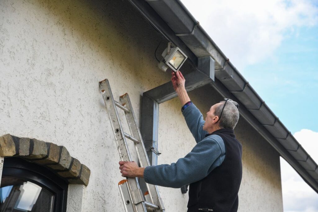 Electrician installing outdoor security light with motion detector at Riverton Home